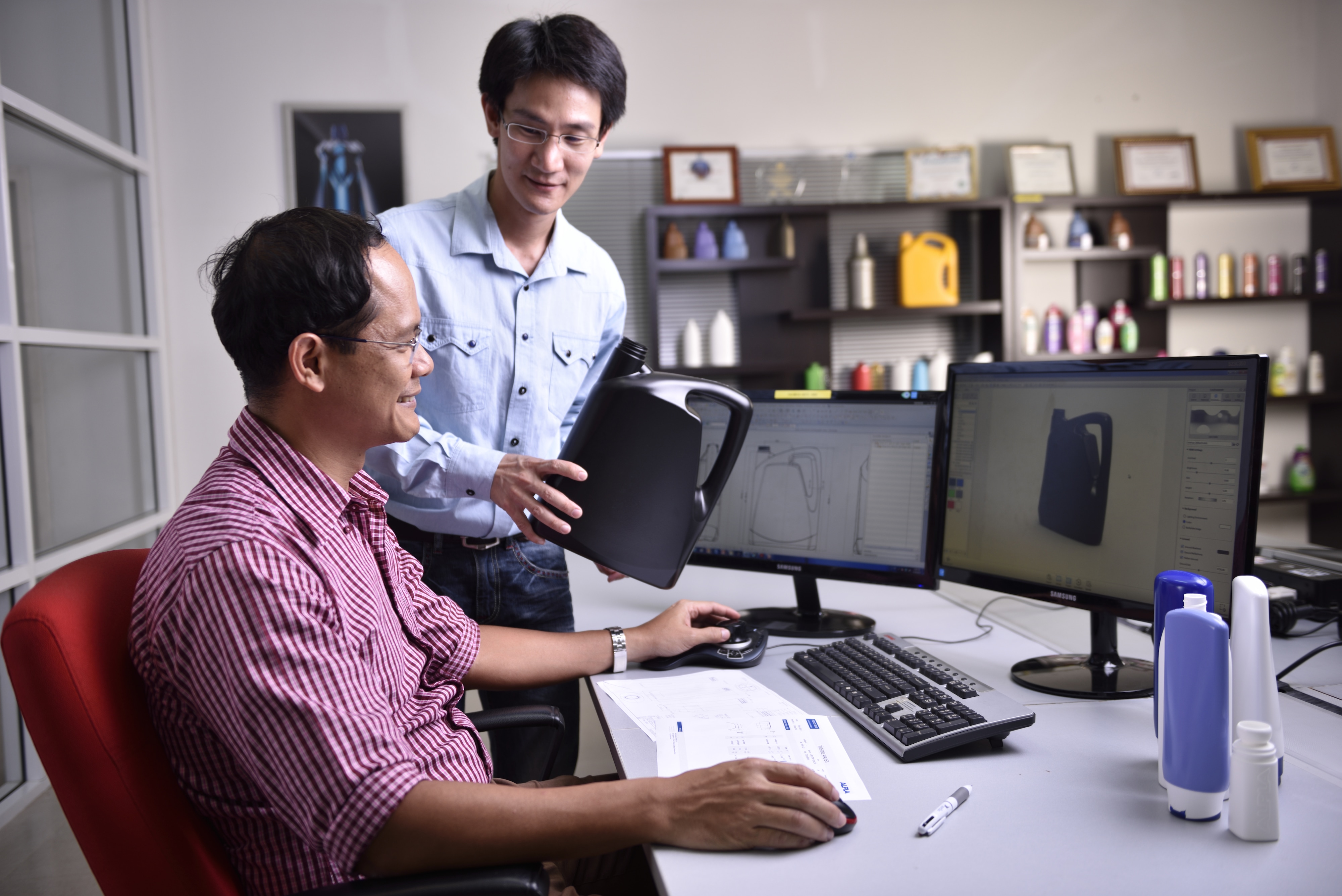 Two men discussing a black plastic container design on a computer screen.