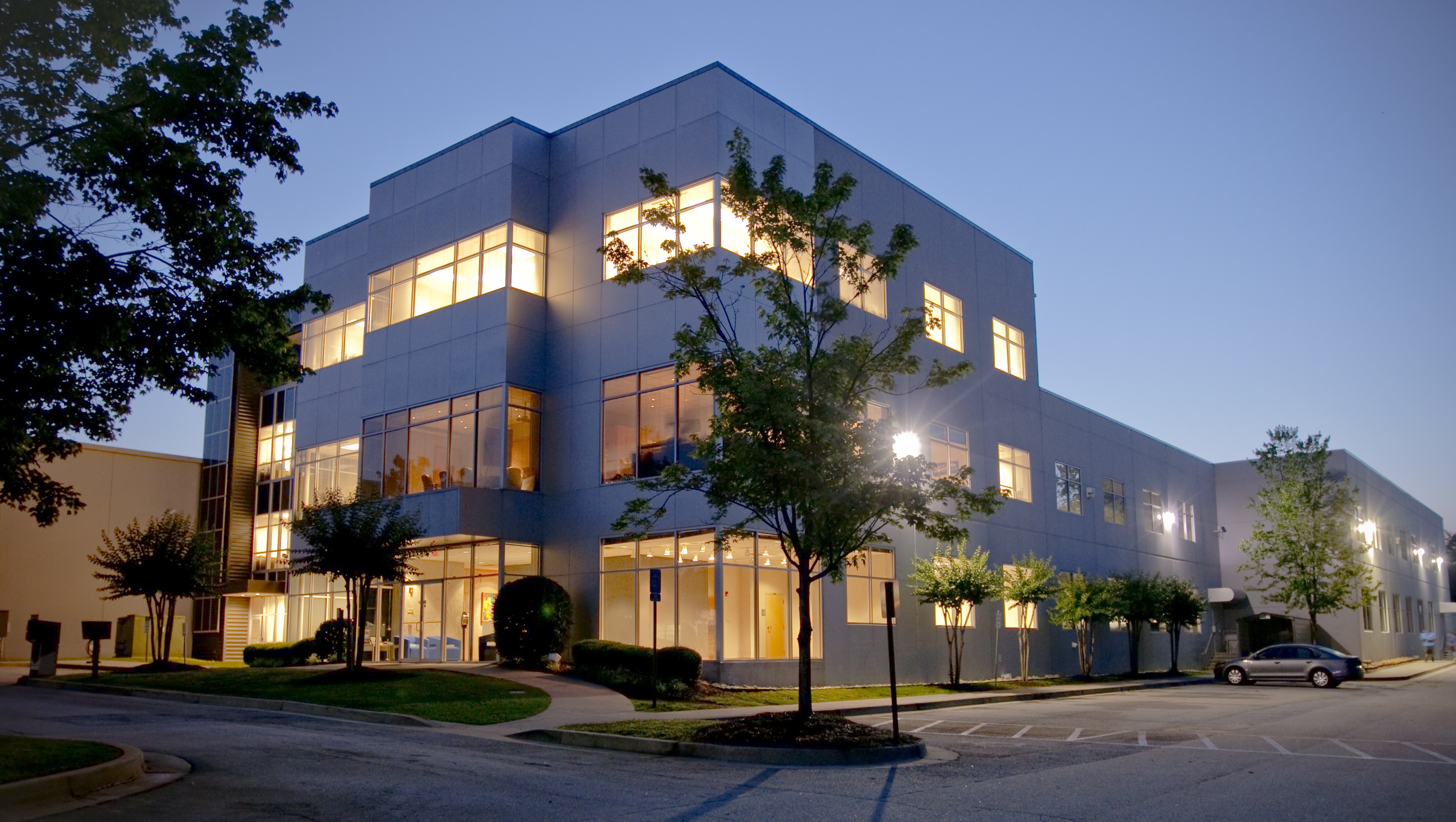 Modern office building at dusk with lit windows and trees.