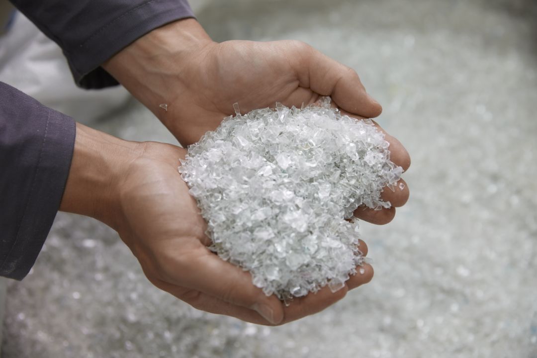 Hands holding clear plastic pellets in a production setting.
