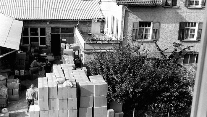 Black and white photo of tall stacks of cardboard boxes in a courtyard.