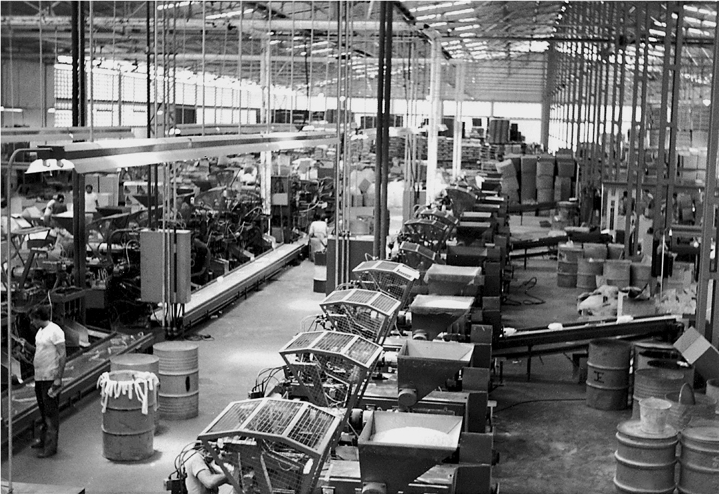 Black and white photo of a busy manufacturing facility with machinery and workers.