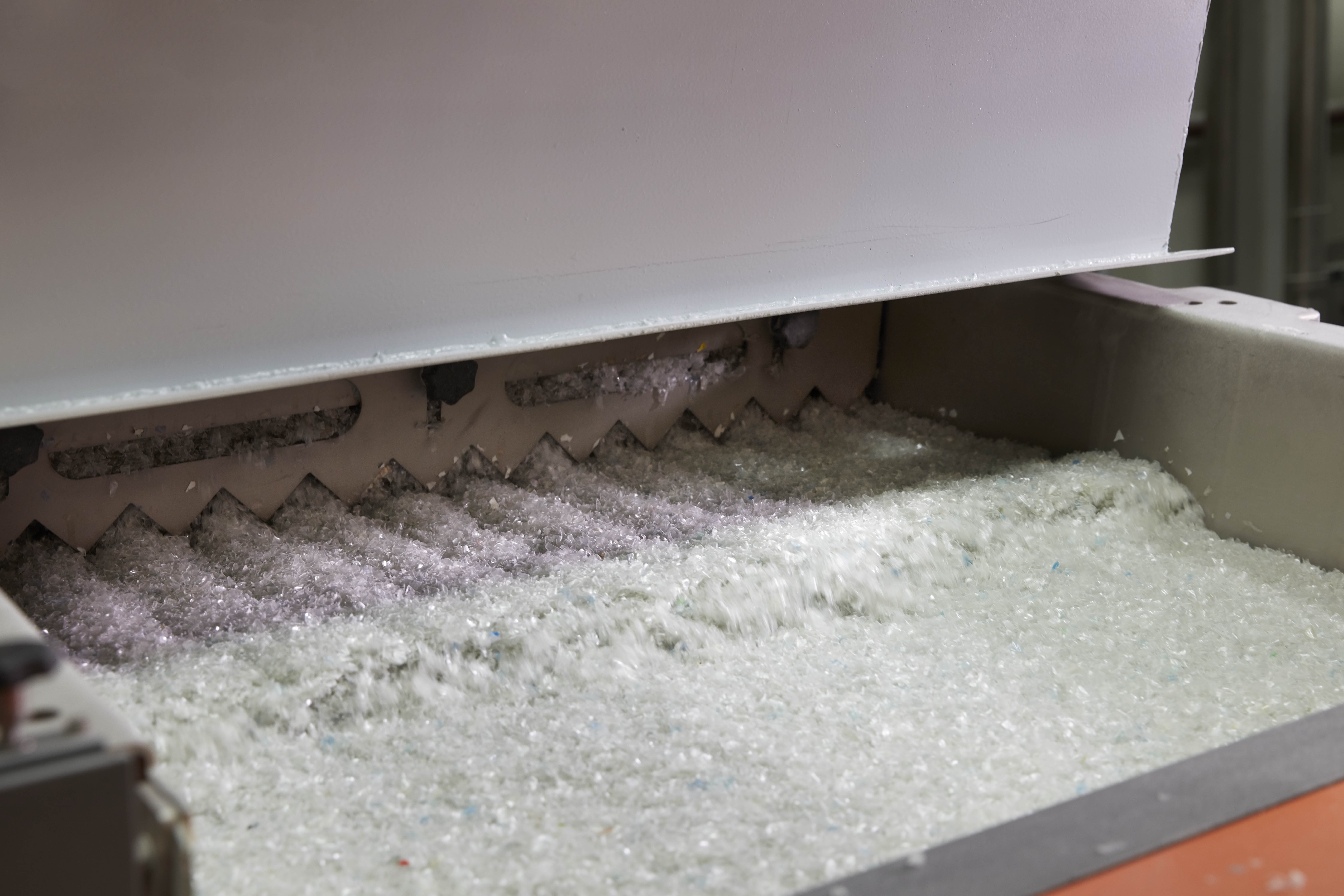Plastic flakes on a conveyor belt in an industrial setting.