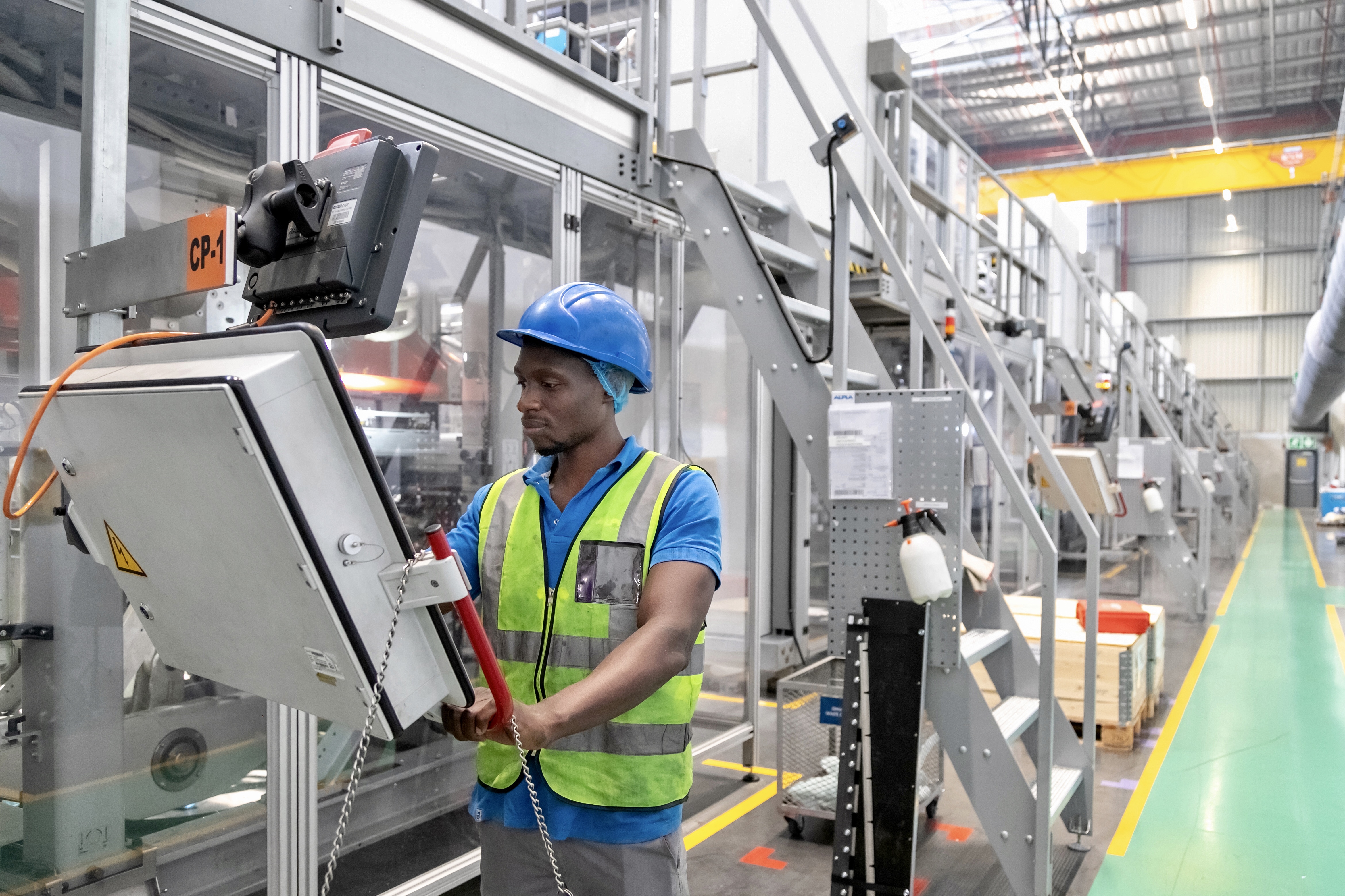 Factory worker in safety gear operating machinery on a production line.