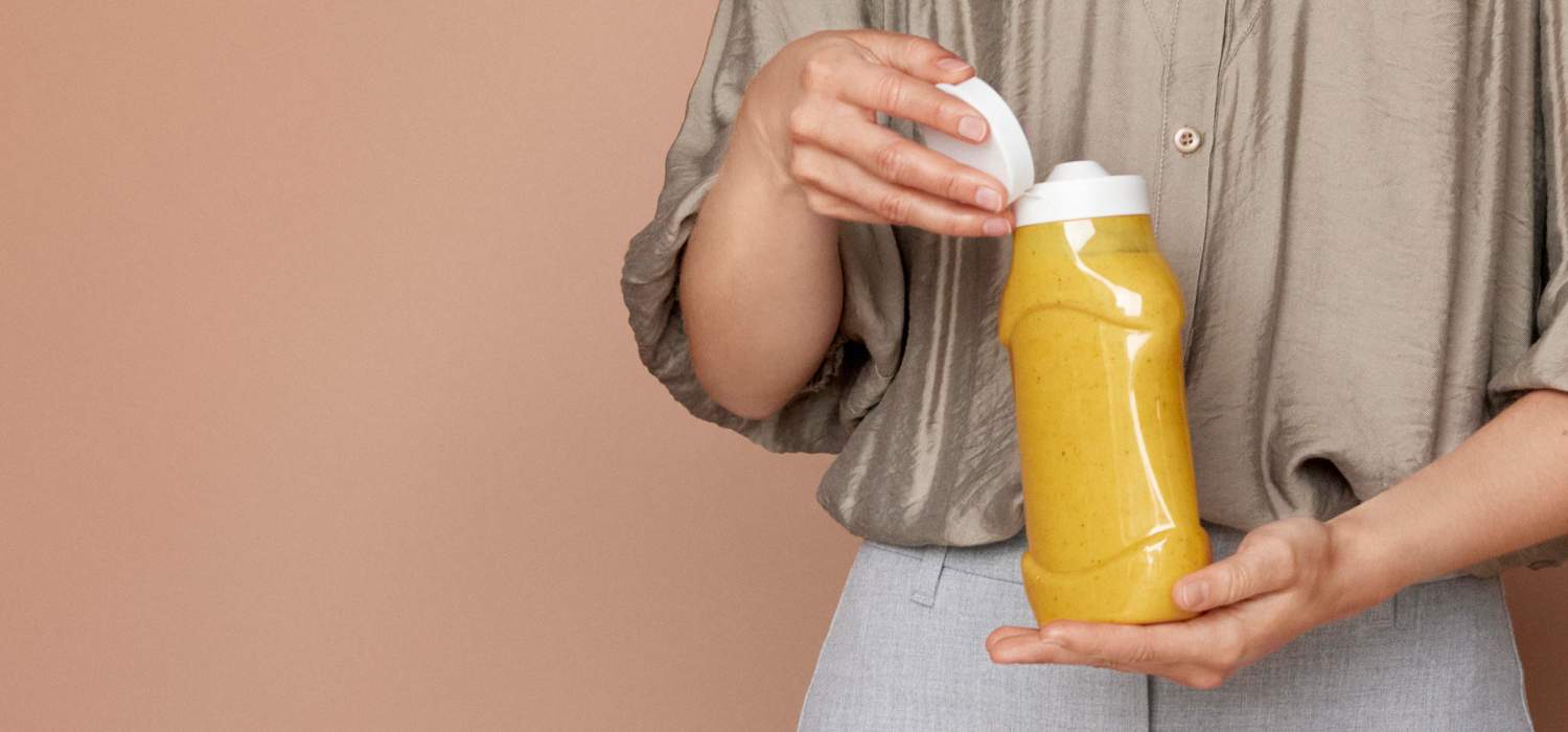 Person holding a yellow bottle with a white cap against a beige background.