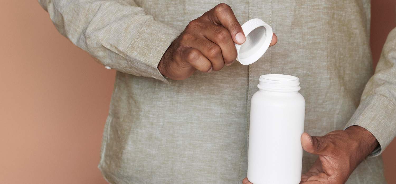 Man opening a white bottle against a brown background.
