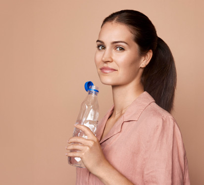 Woman holding a plastic water bottle on a beige background.