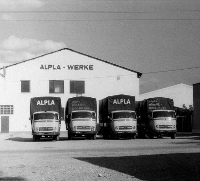 Four ALPLA trucks parked in front of a warehouse, black and white photograph.