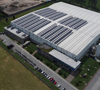 Large industrial facility with solar panels, surrounded by green fields.