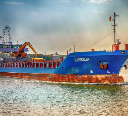 Blue cargo ship on a sunny waterway, with cranes onboard.