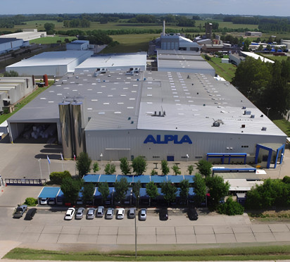 ALPLA factory aerial view with surrounding greenery and parked cars.