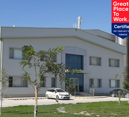 Edifício da ALPLA com um céu azul claro e um primeiro plano gramado.