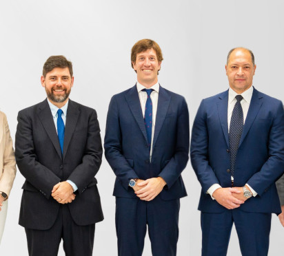 Group of six people in business attire standing against a gray background.