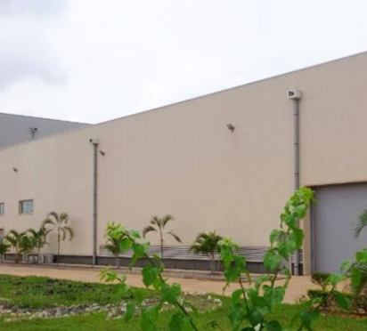 Large beige industrial building with green landscape and cloudy sky.