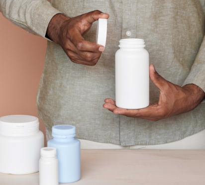 Person opening a white plastic bottle, various containers on a table.