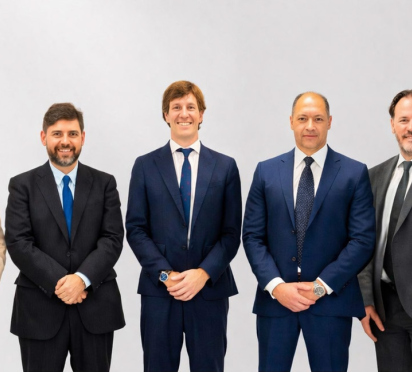 Nove profissionais de negócios em ternos, juntos, sorrindo em um fundo claro.