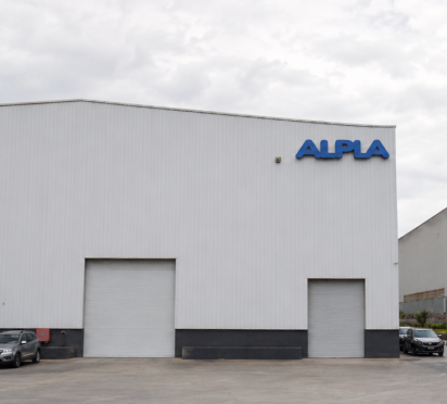 ALPLA facility exterior with parked cars and cloudy sky.