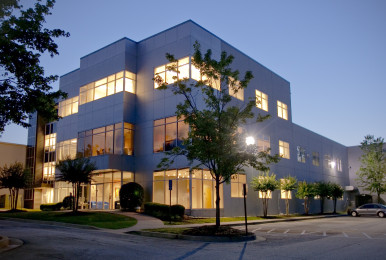 Modern office building at dusk with lit windows and trees.
