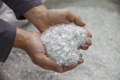 Hands holding clear plastic pellets in a production setting.