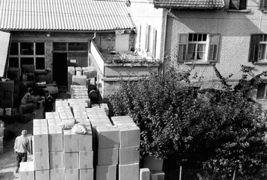 Black and white photo of tall stacks of cardboard boxes in a courtyard.