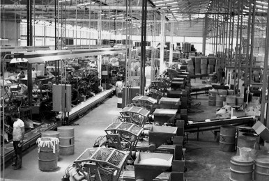 Black and white photo of a busy manufacturing facility with machinery and workers.