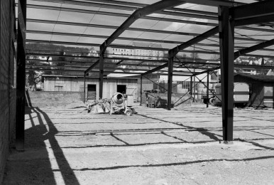 Steel structure under construction with concrete flooring, shadows cast in sunlight.