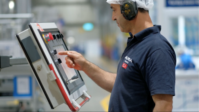 Worker in protective gear operates a touchscreen in a manufacturing facility.