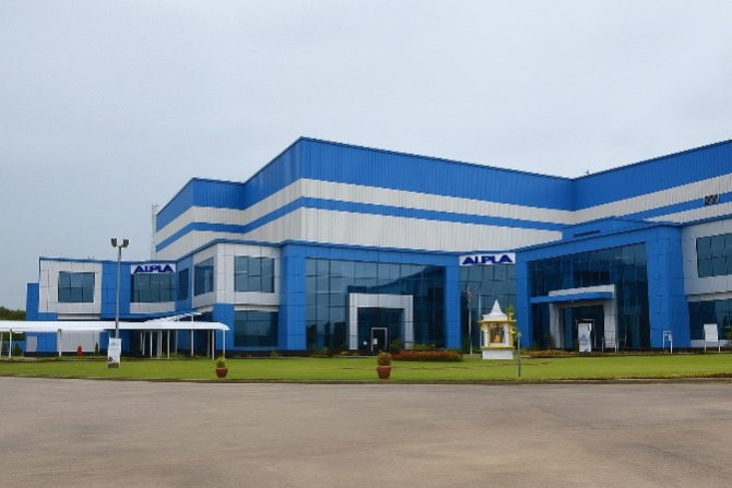 Blue and white ALPLA factory building with large windows and grassy front area.