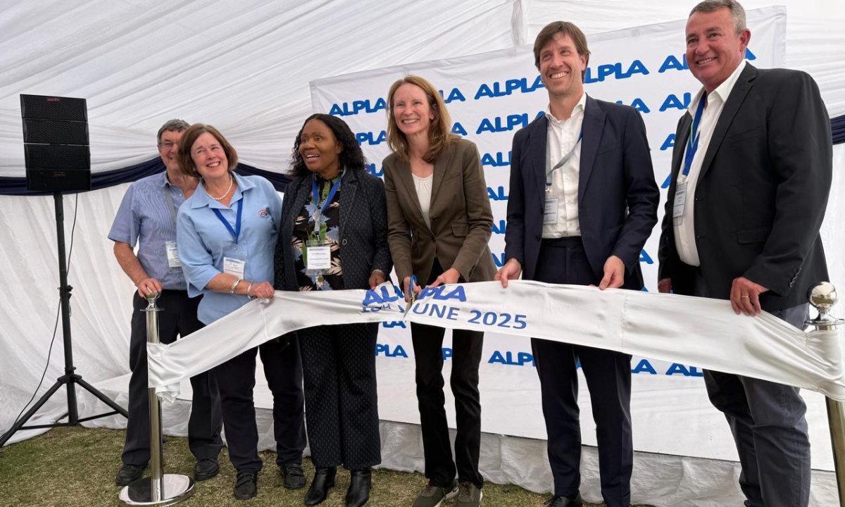 People holding a ribbon at an ALPLA event under a white tent.