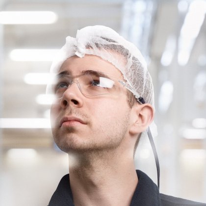 Fabrikarbeiter mit Haarnetz und Schutzbrille in einer industriellen Umgebung.