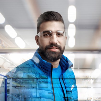 Mann in blauer Jacke vor einem unscharfen industriellen Hintergrund.