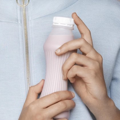 Hands holding a pink, ribbed bottle with a white cap.
