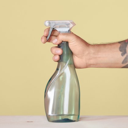 Hand holding a spray bottle against a yellow background.
