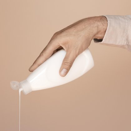 Hand pouring white lotion from a bottle against a beige background.