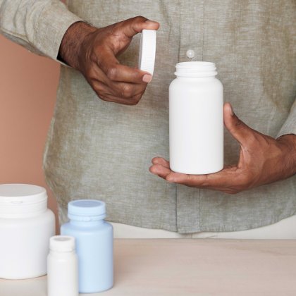 Person opening a white plastic bottle, various containers on a table.