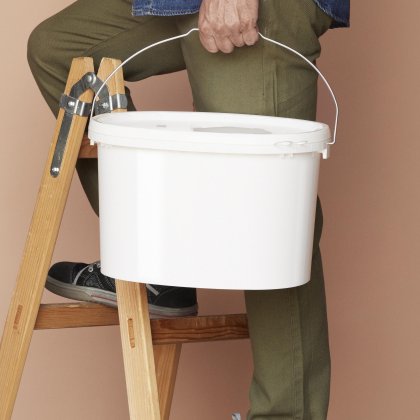 Person carrying a plastic industrial bucket with metal handle for paints, coatings and construction materials.